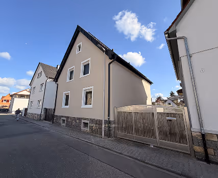 Straßenseite mit zwei dreistöckigen Häusern unter blauem Himmel mit wenigen Wolken.