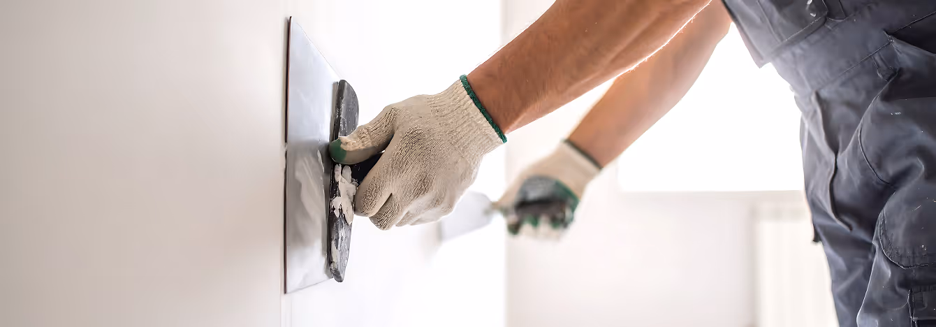 Handwerker mit Handschuhen trägt Spachtelmasse auf eine Wand auf.