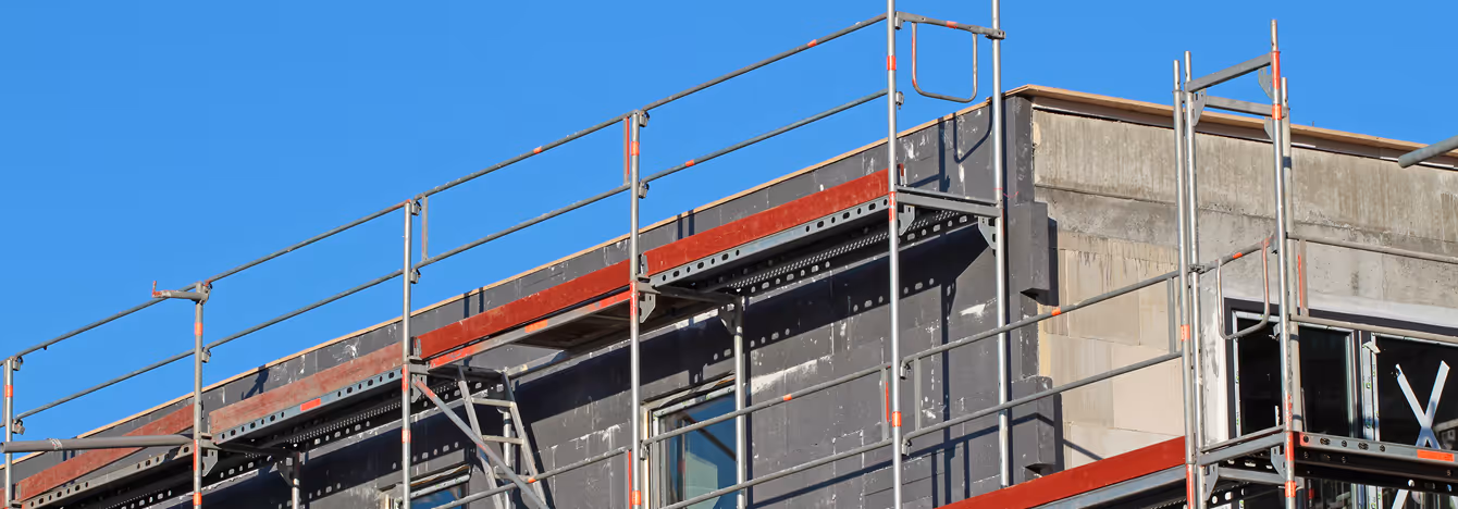 Obere Etage eines Gebäudes mit Baustellengerüst vor blauem Himmel.