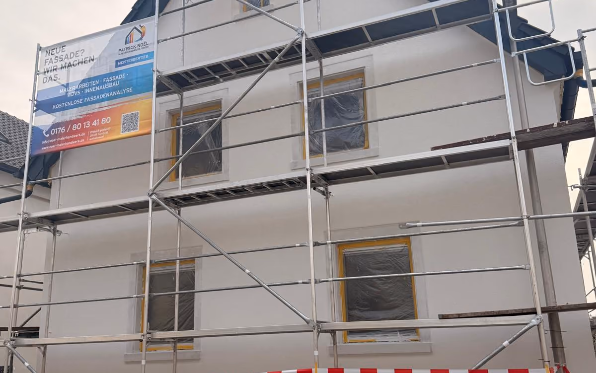 Eingerüstete Hausfassade mit Baustellenbanner von Patrick Noël Malerhandwerk und abgeklebten Fenstern