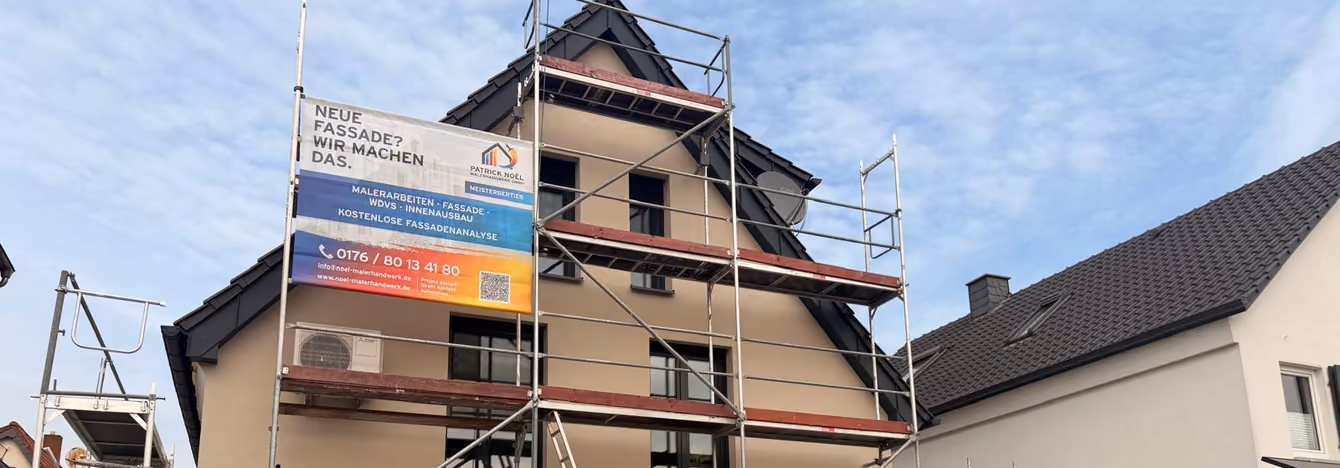 Eingerüstetes Wohnhaus mit Baustellenbanner von Patrick Noël Malerhandwerk während der Fassadenarbeiten