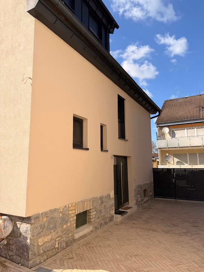 Hofseite eines Wohnhauses mit neuer heller Fassade und Natursteinsockel