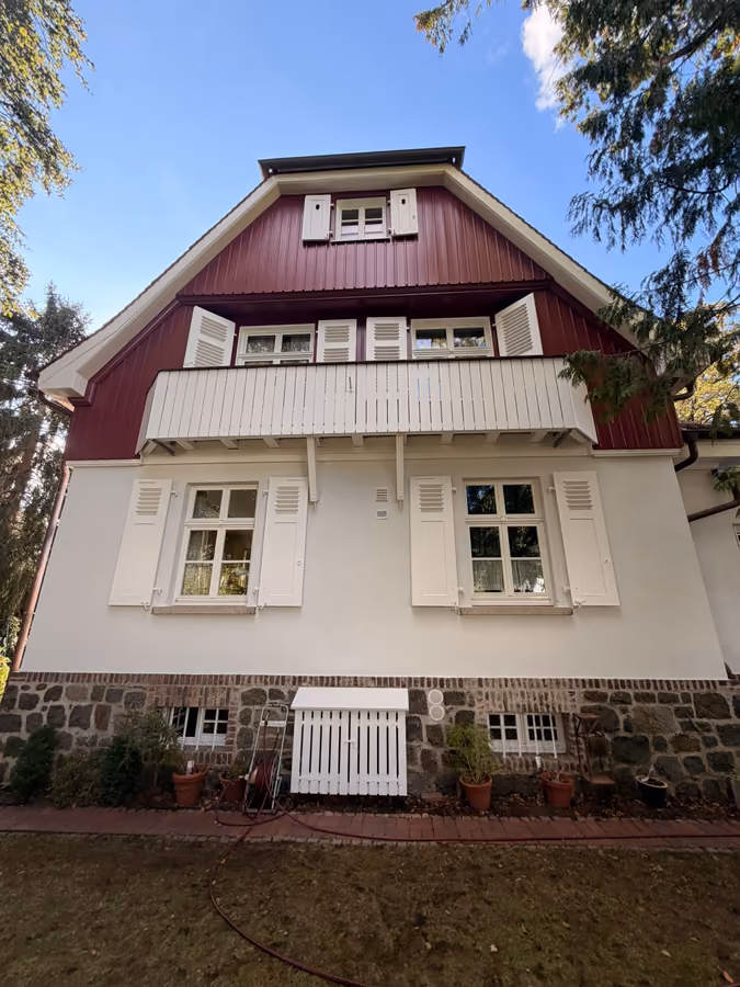 Referenzobjekt: Villa mit rotem Holzgiebel, weißem Balkon und hellen Fensterläden